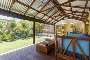 Eine überdachte Terrasse mit Holzboden, einer Sitzecke mit blauen Kissen und verschiedenen K übelpflanzen.