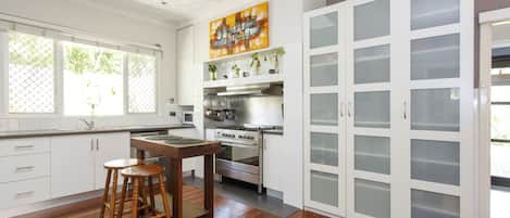A kitchen with white cabinets, a stove, a dining table with stools, and a large window with a view of greenery.