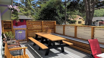A wooden deck with picnic tables and chairs, surrounded by a wooden fence and trees.