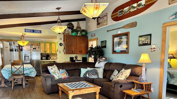 A cozy living room with a sofa, coffee table, and a dining area with chairs. There is a kitchen in the background with a refrigerator and cabinets. - Superb 3-bedroom house with WiFi in Neskowin.   (Neskowin)
