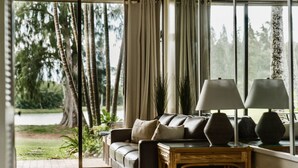 Ein modernes Wohnzimmer mit einer Ledersofa, zwei Lampen und Blick auf einen Park durch große Fenster.