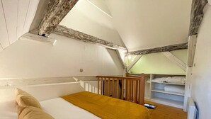 Un dormitorio con techo de madera, una cama con colchón blanco y manta marrón, y suelo de madera.