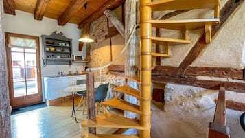 Un escalier en colimaçon dans une pièce rustique aux poutres apparentes et aux murs en pierre.