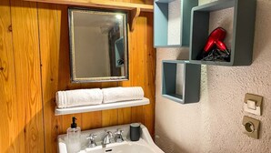 Un baño con pared de madera, un lavabo blanco, un espejo y repisas con artículos de aseo.