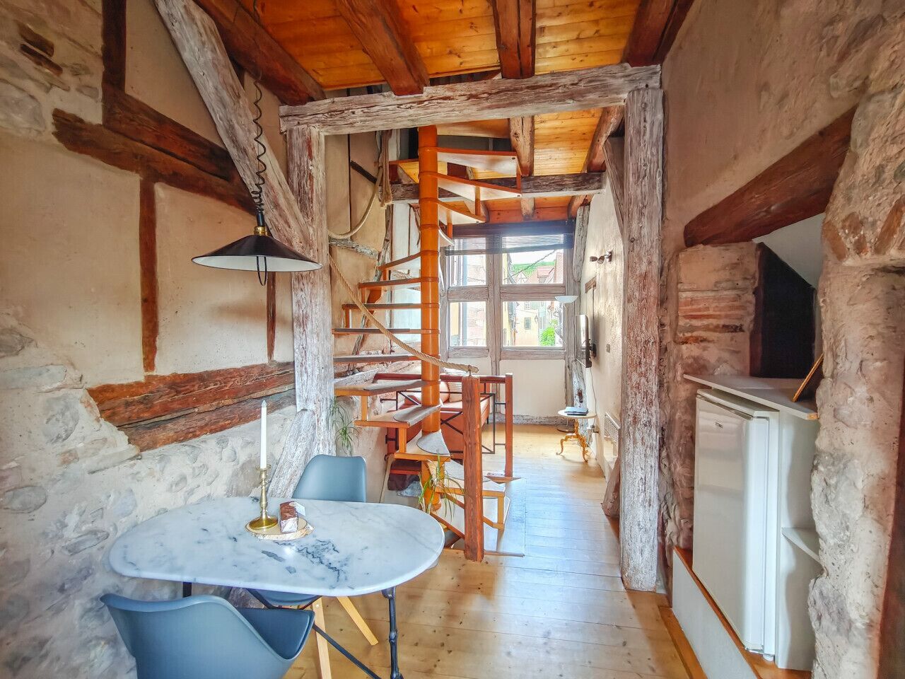 Een rustieke keuken met een houten trap, een eettafel met stoelen en een koelkast.