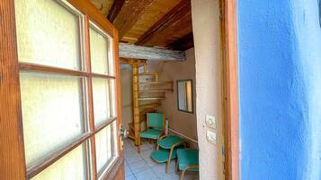 Un couloir étroit avec un escalier en bois, des chaises vertes et un mur bleu.