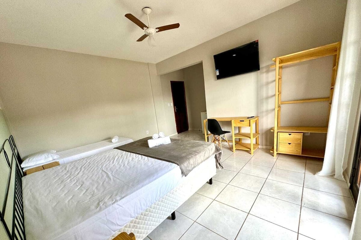 A hotel room with two beds, a desk, a chair, a TV, and a wardrobe.