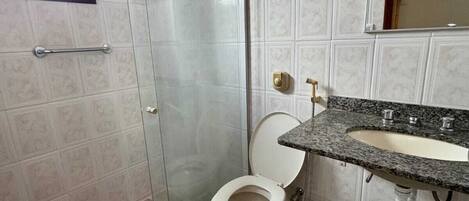 A bathroom with a glass-enclosed shower, a toilet, and a sink with a granite countertop.