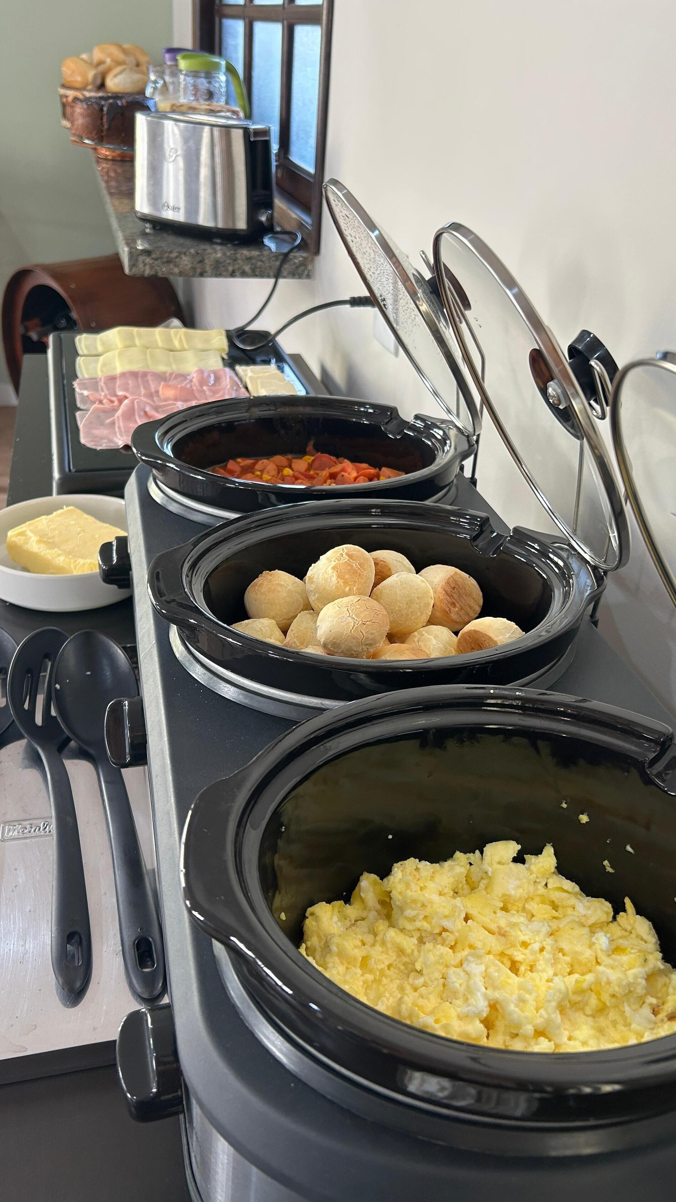 Montaje de bufé con diversos alimentos, entre ellos pan, carnes y huevos revueltos.
