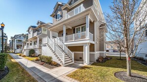 A multi-story residential building with a central staircase, a covered front porch, and a well-maintained lawn.