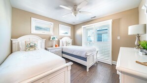 A bedroom with two beds, a ceiling fan, and a window with blinds.