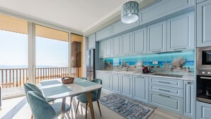 Eine moderne Küche mit hellblauen Schränken, einer großen Insel mit Glastischplatte und Meerblick durch ein Fenster.