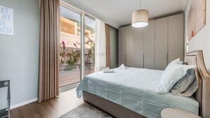 Ein modernes Schlafzimmer mit einem großen Bett, einem Kleiderschrank und Blick auf ein Gebäude sowie Grünflächen.