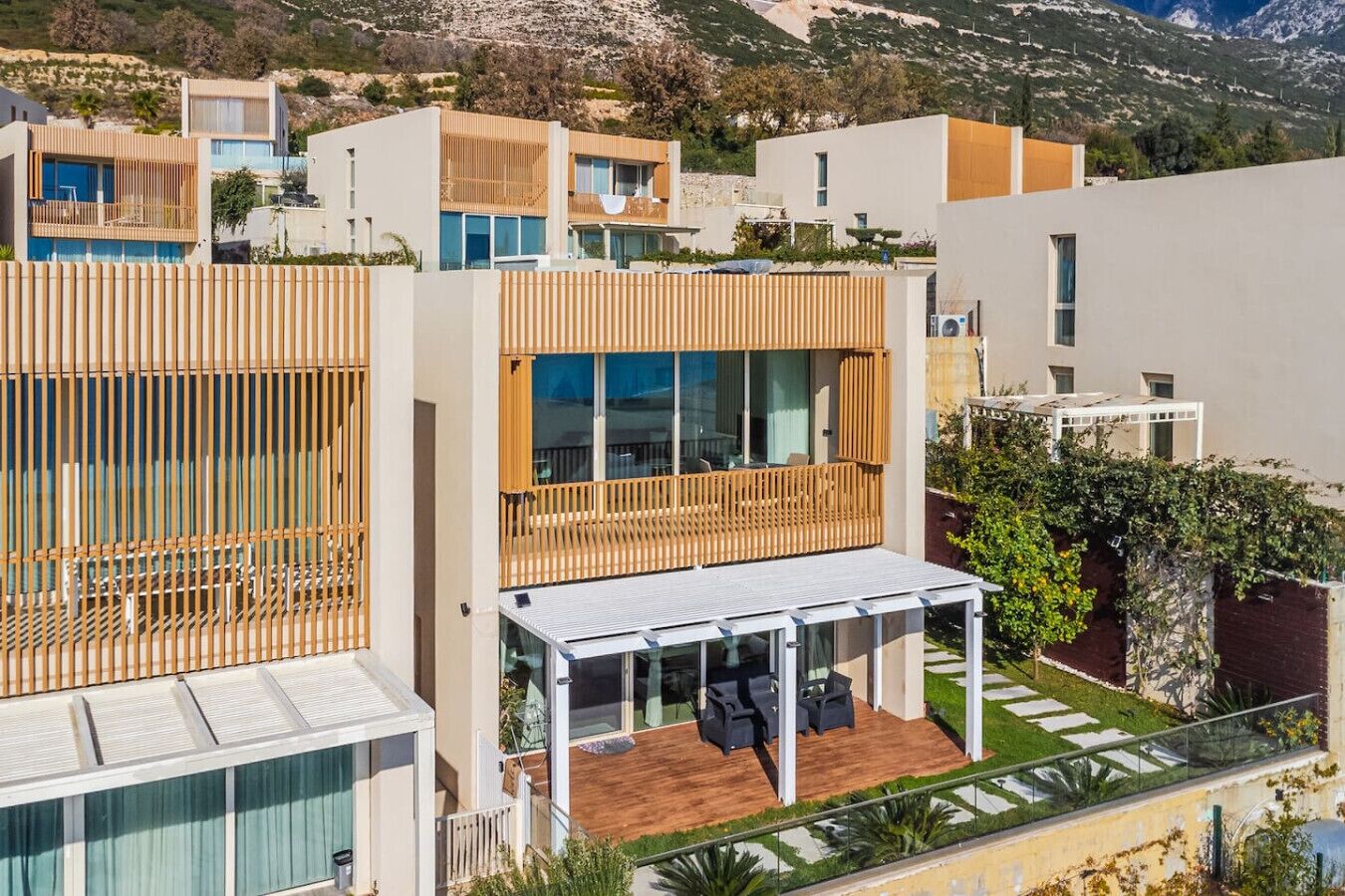 Un edificio residencial moderno con balcón de madera, zona de estar exterior cubierta y vistas del paisaje circundante.