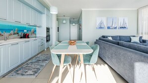 Eine moderne Küche mit hellblauen Schränken, ein Essbereich mit Tisch und Stühlen sowie ein Wohnzimmer mit grauem Sofa.