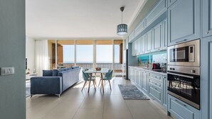 Eine moderne Küche mit hellblauen Schränken, einem Essbereich mit Tisch und Stühlen sowie einem großen Fenster mit Blick auf einen Balkon.
