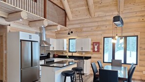 Een moderne keuken met een centraal eiland, roestvrijstalen apparatuur en een eethoek met een groot raam.