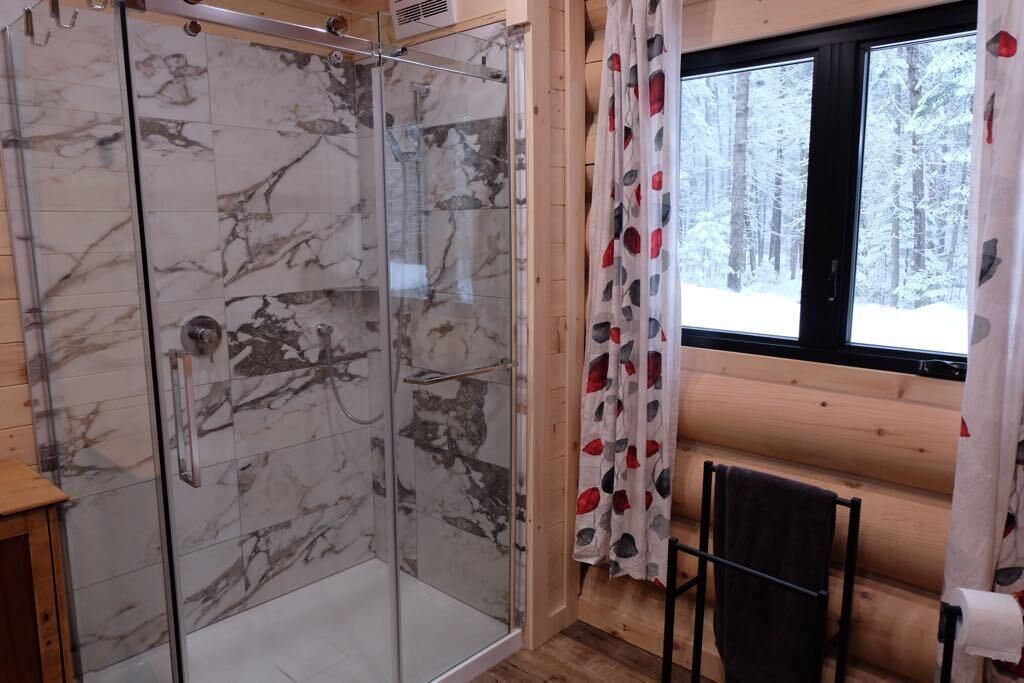 Een glazen douche met marmeren tegels, een houten interieur, een raam met uitzicht op een besneeuwde bossen en een handdoekrek met een handdoek.