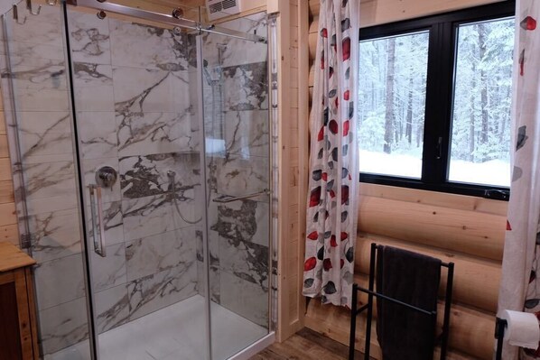 Eine gläserne Dusche mit Marmorfliesen, ein Holzhütten-Interieur, ein Fenster mit Blick auf einen verschneiten Wald und ein Handtuchhalter mit Handtuch.