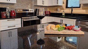 Een moderne keuken met witte kasten, roestvrijstalen apparatuur en een groot eiland met een wijnglas en vers fruit.