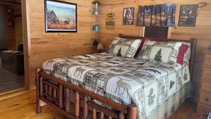 Une pièce de cabane en bois comprenant un lit, un tableau encadré représentant un cerf, un panneau d’avertissement et une lampe.