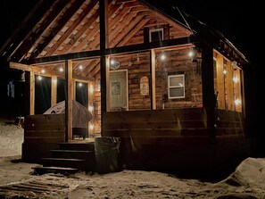 A wooden cabin with a porch, illuminated by string lights, and a 'Welcome' sign. - Cozy cabin in brilliant Lewis with WiFi, AC (Lewis)