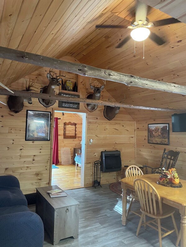 A cabin interior with wooden walls, mounted deer heads, a dining table with chairs, a ceiling fan, and a fireplace. - Cozy cabin in brilliant Lewis with WiFi, AC (Lewis)