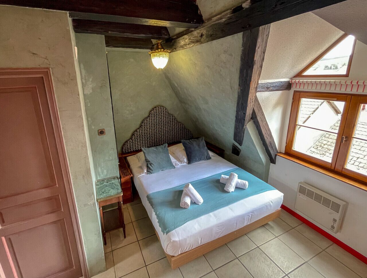 Ein Schlafzimmer mit Bett, Kissen, einem Nachttisch, einer Lampe, einem Fenster und einer Heizung.