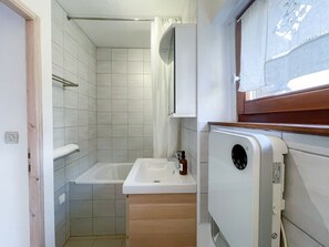 Un baño pequeño con un lavamanos blanco, zona de ducha y un mueble auxiliar.