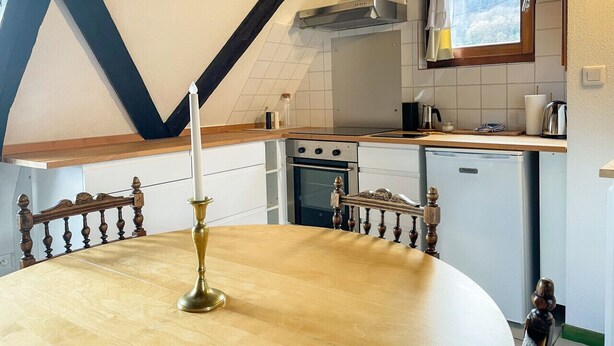 A kitchen with a wooden dining table, a chandelier, and a window with a view of trees. - La Maison Bleue - Historic house in the heart of Riquewihr. 5 guest apartment (Riquewihr)