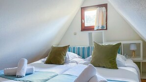 A bedroom with a bed, pillows, a nightstand, a lamp, and a window with curtains. - La Maison Bleue - Historic house in the heart of Riquewihr. 5 guest apartment (Riquewihr)