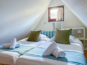 Een slaapkamer met een bed, kussens, een nachtkastje, een lamp en een raam met gordijnen.