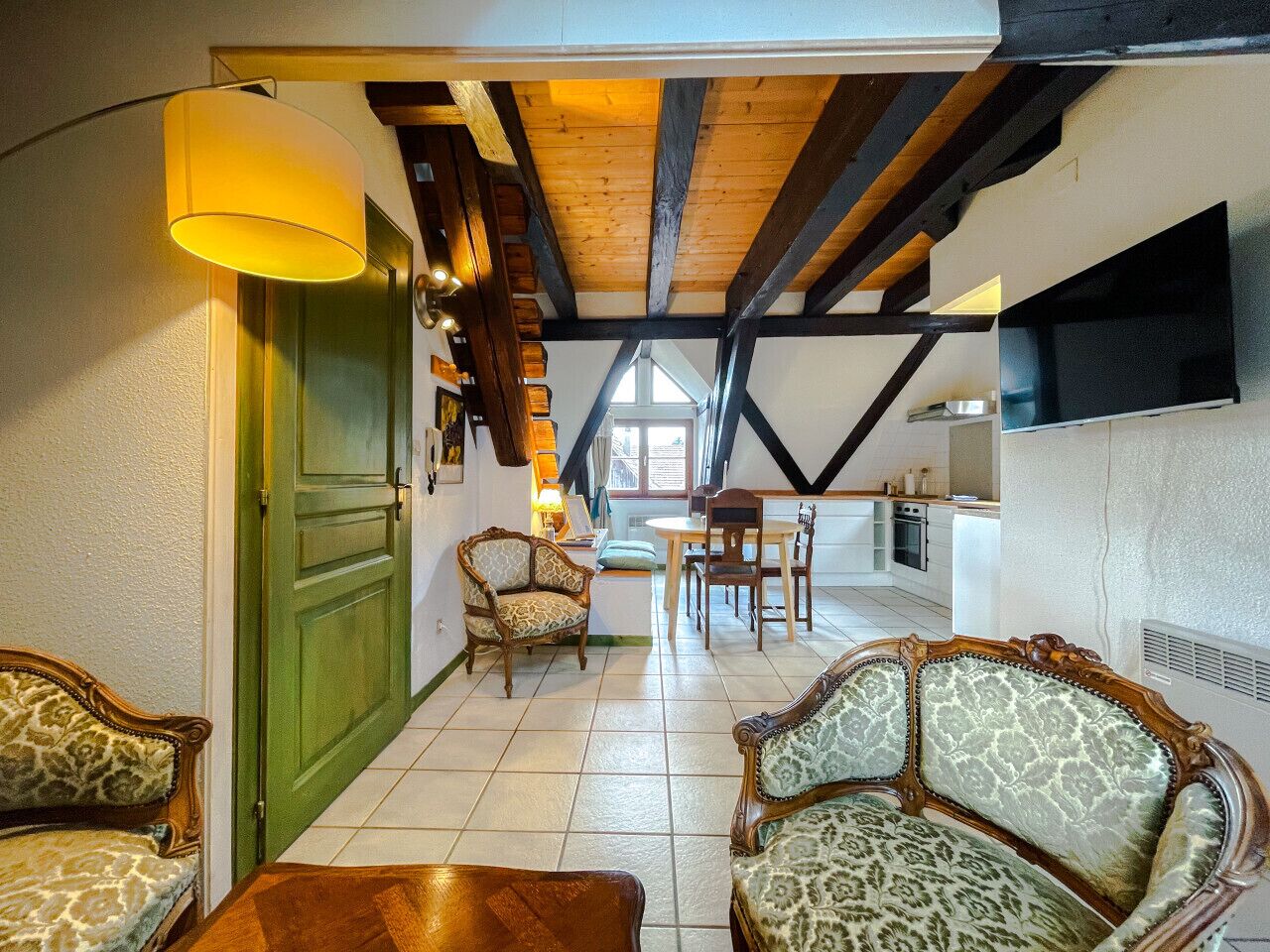 Ein gemütliches Wohnzimmer mit einer grünen Tür, einem Essbereich mit Tisch und Stühlen sowie einer Küche im Hintergrund.