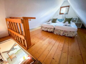 Une chambre avec un plancher en bois, deux lits avec une literie à motifs floraux, une échelle en bois et une petite fenêtre avec des rideaux.