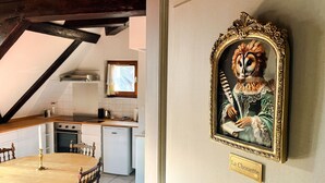 A dining area with a wooden table and chairs, a kitchen in the background, and a framed painting on the wall. - La Maison Bleue - Historic house in the heart of Riquewihr. 5 guest apartment (Riquewihr)