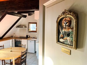 Een eethoek met een houten tafel en stoelen, een keuken op de achtergrond en een gekaderd schilderij aan de muur.