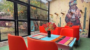A dining area with red chairs and a table, large windows, and a mural on the wall. - Anido Hotel (Ollantaytambo)