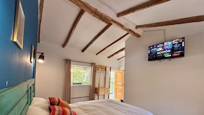 A bedroom with a bed, a TV mounted on the wall, a window with curtains, and a wooden door. - Anido Hotel (Ollantaytambo)