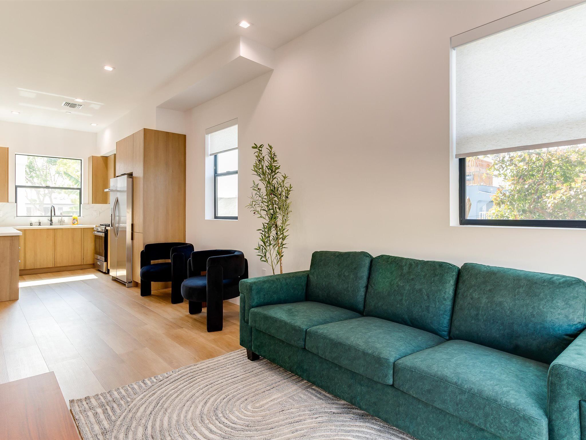 Una sala de estar moderna con un sofá verde, un comedor con mesa de madera y una cocina con refrigerador y armarios.