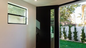 A modern interior with a black door, a small window, and a view of a green lawn and white fence outside. - Modern Luxe Retreat#3 Three-Bedroom (Los Angeles)