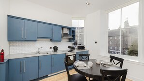 A modern kitchen with blue cabinets, a white countertop, and a dining table with chairs.