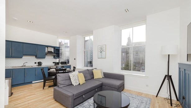A modern apartment with a kitchen, a grey sofa, a round coffee table, and a city view.