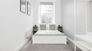 A minimalist bedroom with a white bed, a window, and a radiator.