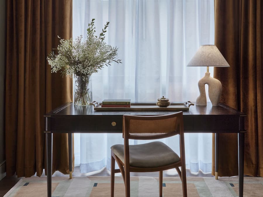 Una habitación con escritorio, silla y ventana con cortinas translúcidas.