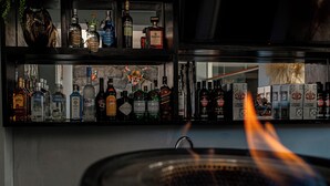 Zona de bar con estantes llenos de botellas de licor y una parrilla con llamas.