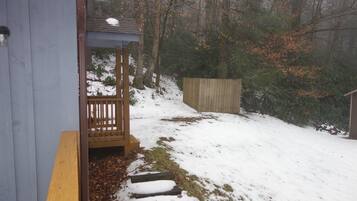 Een houten terras leidt naar een overdekt gebied met uitzicht op een besneeuwd landschap en bomen.