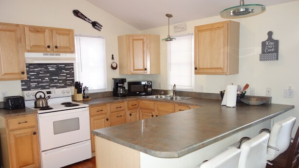 A kitchen with wooden cabinets, a stainless steel sink, a stove, and a bar area with white chairs. - Mountain home in Newland (Newland)