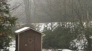 A wooden shed with a wreath on the door, surrounded by snow-covered ground and trees. - Mountain home in Newland (Newland)