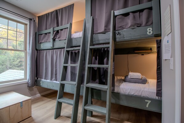 Quarto com beliches, escada, camas numeradas e janela com cortinas.