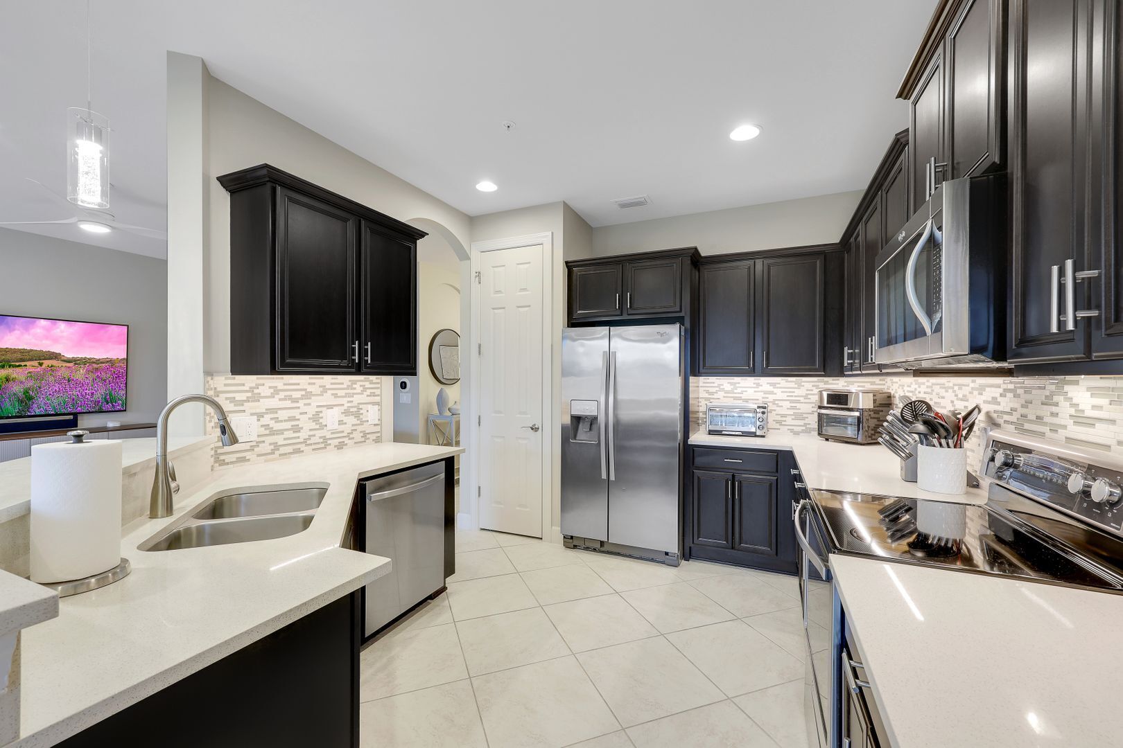 A modern kitchen with dark cabinets, stainless steel appliances, and a tiled backsplash.